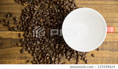 Flat design is showing dark roasted beans and red-handled white coffee cup resting on wood tabletop Flat design is showing dark roasted beans and red-handled white coffee cup resting on wood tabletop 133599824