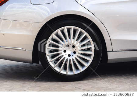 Luxury silver car with detailed alloy wheel parked on smooth pavement in sunlight Luxury silver car with detailed alloy wheel parked on smooth pavement in sunlight 133600687