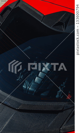 Red sports car with a visible engine through the rear window in bright sunlight 133600794