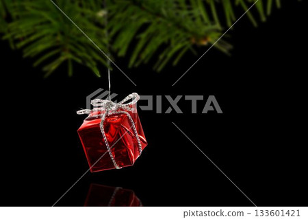 Red metallic vector gift ornament is hanging from fir needles with silver ribbon on black backdrop 133601421