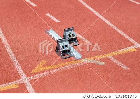 metal starting block is resting on red track, flat vector design showing white lanes, yellow arrow 133601779