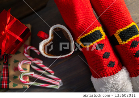 Woman legs with christmas socks and home interior with fireplace and dark wall background. Free space for your decoration. Woman legs with christmas socks and home interior with fireplace and dark wall background. Free space for your decoration. 133602011