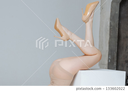 A woman's legs in beige high-heeled shoes, raised in an elegant pose, wearing a nude swimsuit. A girl's sexy butt in a nude swimsuit. Professional studio shoot of a model. A woman's legs in beige high-heeled shoes, raised in an elegant pose, wearing a nude swimsuit. A girl's sexy butt in a nude swimsuit. Professional studio shoot of a model. 133602022