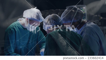Operating surgeons wearing scrubs working under surgical light in operating room with monitors 133602414