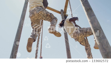 Climbing military partners navigating outdoor obstacle course, with wooden poles and climbing ropes Climbing military partners navigating outdoor obstacle course, with wooden poles and climbing ropes 133602572