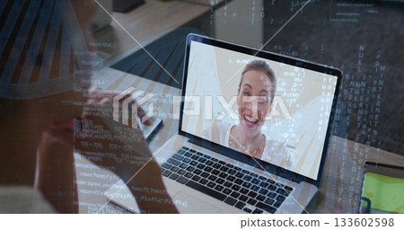 Holding smartphone viewing colleague smiling on laptop screen at home office desk, notebook and pen 133602598