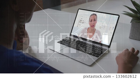 Woman wearing blue top viewing charts on silver laptop in home office, with gray potted plant 133602612