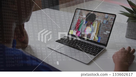 Watching person leaning on desk in home office, viewing silver laptop showing color wheel by rack 133602617