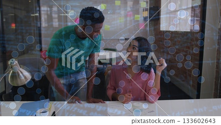 Coworkers reviewing documents and discussing data overlays in modern office, with desk lamp 133602643