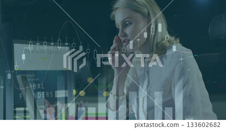 Talking businesswoman in blouse using smartphone and laptop in office at night, monitoring charts 133602682