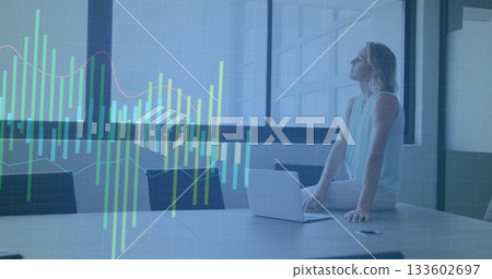 Woman sitting on table by office window viewing chart overlay with laptop smartphone, copy space 133602697