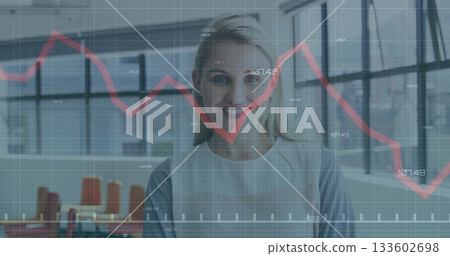 Standing professional in blazer showing data in modern office with grid windows, red graph overlay 133602698