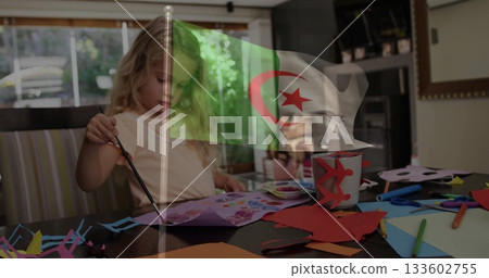 Painting girl applying colors with brush on paper cutouts at dining table, with Algerian flag Painting girl applying colors with brush on paper cutouts at dining table, with Algerian flag 133602755