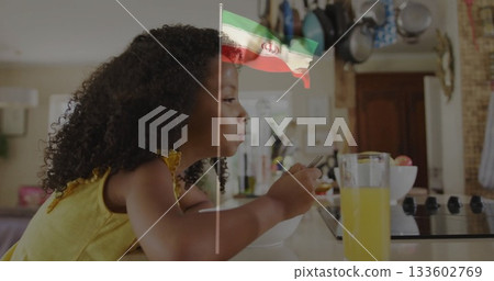 Leaning girl in yellow top using spoon eating from bowl at home countertop, with orange juice Leaning girl in yellow top using spoon eating from bowl at home countertop, with orange juice 133602769