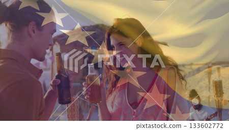 Toasting couple holding beer bottles clinking near beach cabana at sunset, with tiki torch 133602772
