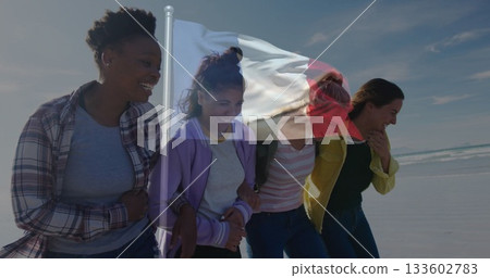 Walking four friends linking arms at sandy beach, with translucent French flag overlay 133602783