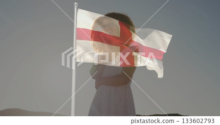 Facing woman wearing white sleeveless dress on barren hillside at dawn, with St George's cross flag Facing woman wearing white sleeveless dress on barren hillside at dawn, with St George's cross flag 133602793