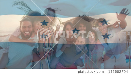 Posing group of eight friends laughing on sandy beach at sunset under straw umbrella, palm fronds 133602794