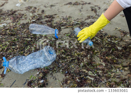 volunteer collecting plastic bottles on a polluted beach, highlighting ocean pollution, waste problem, environmental protection and coastal cleanup action. 133603081