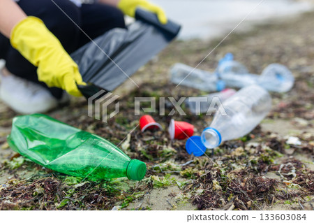 volunteer collecting plastic bottles on a polluted beach, highlighting ocean pollution, waste problem, environmental protection and coastal cleanup action. volunteer collecting plastic bottles on a polluted beach, highlighting ocean pollution, waste problem, environmental protection and coastal cleanup action. 133603084