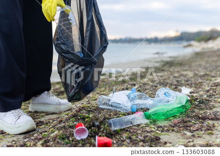 Volunteer collecting plastic waste during beach cleanup, removing litter and protecting the shoreline environment. Volunteer collecting plastic waste during beach cleanup, removing litter and protecting the shoreline environment. 133603088