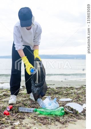Volunteer collecting plastic waste during beach cleanup, removing litter and protecting the shoreline environment. 133603089