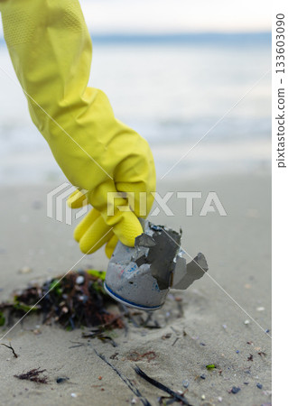 volunteer picking up a crushed metal can during beach cleanup, highlighting pollution, waste problem, ecology, coastal protection and environmental awareness. volunteer picking up a crushed metal can during beach cleanup, highlighting pollution, waste problem, ecology, coastal protection and environmental awareness. 133603090