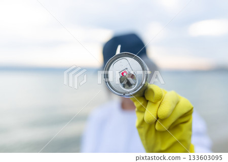 volunteer showing a collected metal can during beach cleanup, highlighting pollution, ecology, environment protection, sustainability and coastal awareness. 133603095