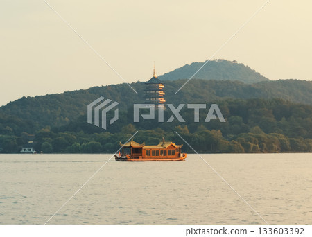 Wooden tourist boat navigate west lake in Hangzhou, China near pagoda temple on hill at dusk 133603392
