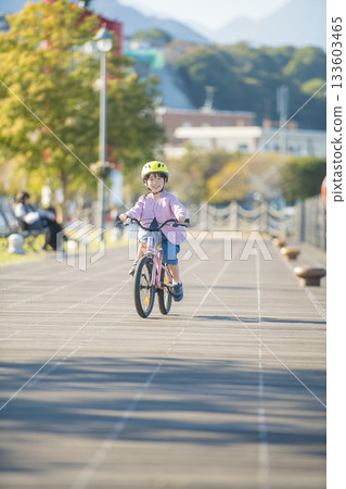 Bright autumn outdoor cycling scene with kindergarten girl running on wooden deck Bright autumn outdoor cycling scene with kindergarten girl running on wooden deck 133603465