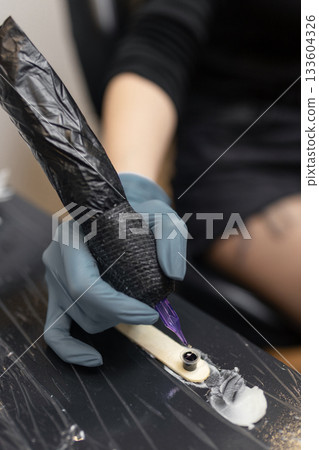 tattoo artist preparing a tattoo machine, dipping the needle into black ink before starting the tattooing process. tattoo artist preparing a tattoo machine, dipping the needle into black ink before starting the tattooing process. 133604326
