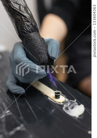 tattoo artist in gloves holding a tattoo machine during a session, preparing tools in a professional studio environment. 133604363