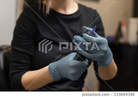 tattoo artist in gloves preparing a tattoo machine, attaching a sterile needle cartridge before a session in a professional studio. tattoo artist in gloves preparing a tattoo machine, attaching a sterile needle cartridge before a session in a professional studio. 133604380