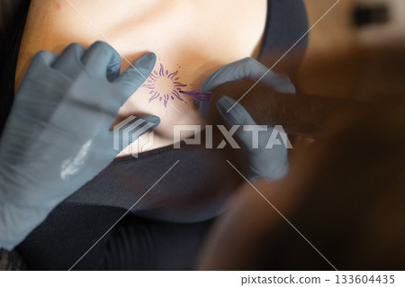 tattoo artist working on a woman chest design in a studio, showing the process of professional tattooing, precision, sterile gloves and cosmetic procedure atmosphere. tattoo artist working on a woman chest design in a studio, showing the process of professional tattooing, precision, sterile gloves and cosmetic procedure atmosphere. 133604435