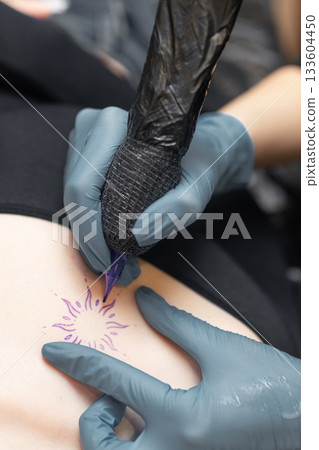 tattoo artist working on a woman chest design in a studio, showing the process of professional tattooing, precision, sterile gloves and cosmetic procedure atmosphere. 133604450