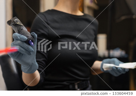 tattoo artist in gloves holding a tattoo machine during a session, preparing tools in a professional studio environment. tattoo artist in gloves holding a tattoo machine during a session, preparing tools in a professional studio environment. 133604459