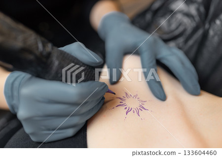 close-up of a tattoo artist outlining a sun design on a client skin, showing the precision of the tattoo process, sterile gloves, and professional equipment. 133604460