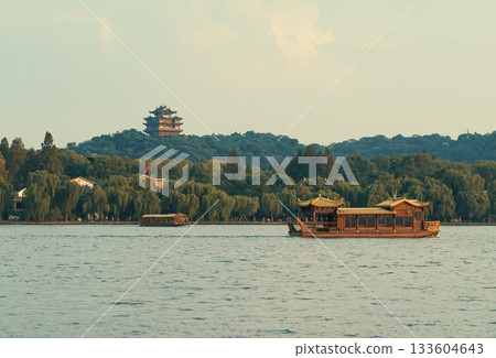 Wooden tourist boats navigate west lake in Hangzhou, China near pagoda temple on hill at dusk Wooden tourist boats navigate west lake in Hangzhou, China near pagoda temple on hill at dusk 133604643