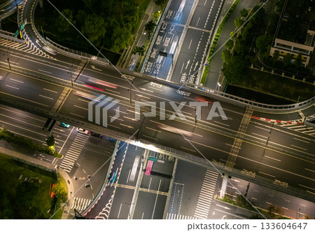 Aerial view of a busy highway intersection at night in an urban area, with moving car light trails. Aerial view of a busy highway intersection at night in an urban area, with moving car light trails. 133604647
