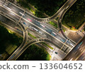 Aerial view of a busy highway intersection at night in an urban area, with moving car light trails. 133604652