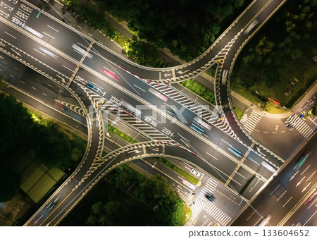 Aerial view of a busy highway intersection at night in an urban area, with moving car light trails. 133604652