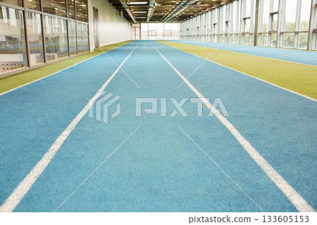 Three blue lined lanes are stretching across gym under beams, lights, flanking glass walls, turf 133605153