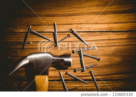 Flat graphic showing metal claw hammer with wooden handle resting on plank scattered with nails 133605330