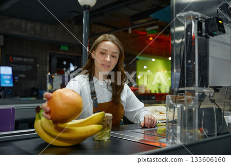 A woman cashier holds an orange and bananas at a store checkout A woman cashier holds an orange and bananas at a store checkout 133606160