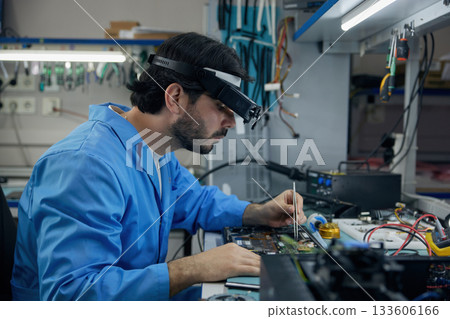Technician man soldering technician dressed in a blue lab coat is diligently repairing a laptop Technician man soldering technician dressed in a blue lab coat is diligently repairing a laptop 133606166