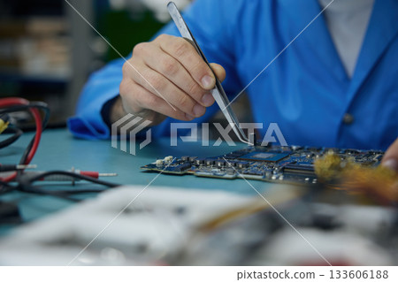 An individual is carefully repairing a motherboard using soldering iron An individual is carefully repairing a motherboard using soldering iron 133606188
