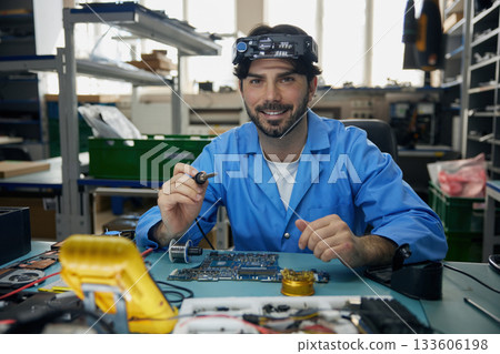 A man soldering technician is diligently working on a computer motherboard 133606198