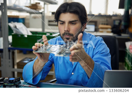 A man worker is wearing a blue shirt holding a motherboard in his hands A man worker is wearing a blue shirt holding a motherboard in his hands 133606204