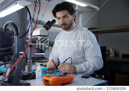 A man worker is focused on working with a motherboard 133606206