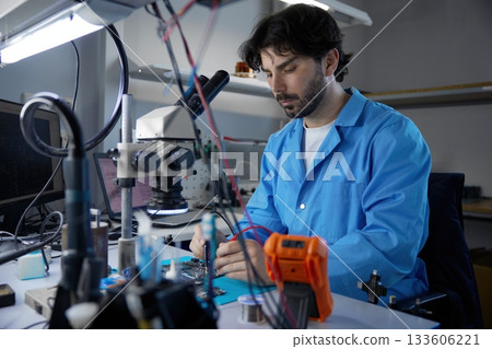 Technician actively engaged in critical work on circuit board while observing under a microscope Technician actively engaged in critical work on circuit board while observing under a microscope 133606221